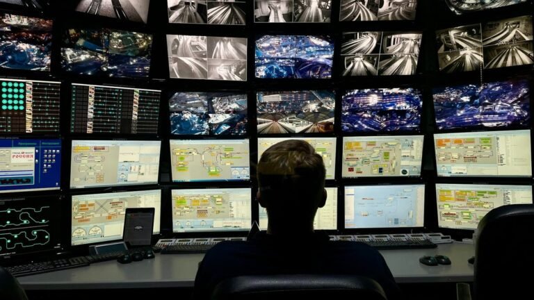 Operador diante de parede de monitores em centro de operação