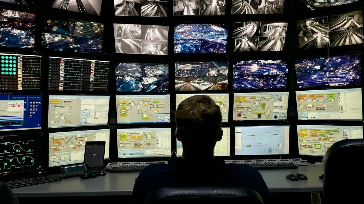 Operador diante de parede de monitores em centro de operação